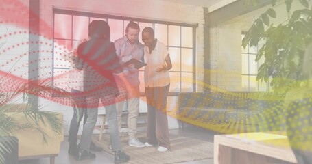 Viewing tablet, four colleagues leaning in at loft workspace in smart casual outfits, with plants