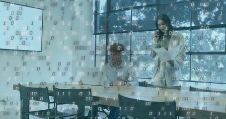 Talking office duo in blazer and shirt holding papers, phone while typing on laptop, binary overlay