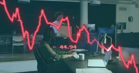 Typing female analyst in light blouse at monitor in office, colleague holding box, red graph -44
