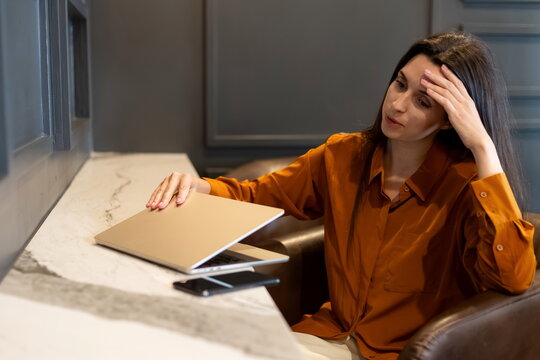 Tired woman closing her laptop in a modern workspace, showing stress and fatigue during remote work, expressing frustration and burnout in a contemporary office environment.