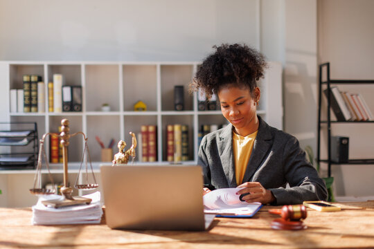 A woman in afro hair paralegal immersed in work at a law office, surrounded by paperwork and legal documents.
