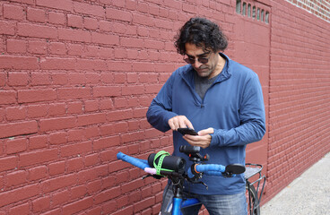 man in sunglasses checking on his bicycle (tire pressure bike maintenance) casual clothes commuter brick wall background urban cycling cyclist biker rider road mountain touring brakes handlebars nyc u