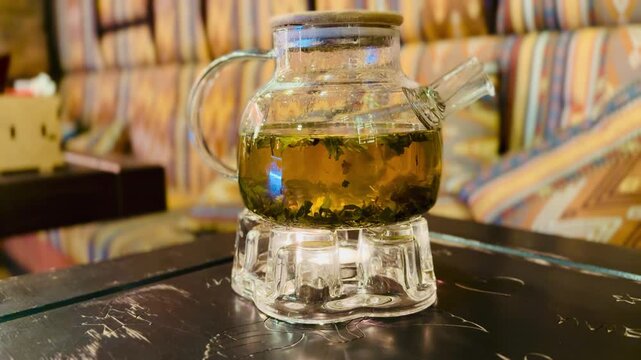 Glass Teapot And Two Teacups With Steaming Herbal Green Tea On Black Marble Tray Surrounded By Patterned Cushions Warm Ambient Lighting Cozy Slow Living Vibe Ideal For Tea Tasting.