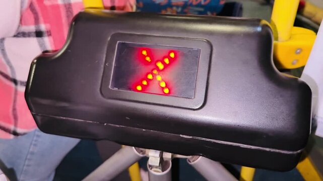 Bus payment gate indicator showing red X to green arrows, closeup of black plastic housing with led matrix, yellow pole and passenger in plaid shirt visible, urban transit