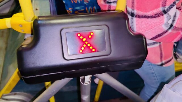 Bus payment gate indicator showing red X to green arrows, closeup of black plastic housing with led matrix, yellow pole and passenger in plaid shirt visible, urban transit