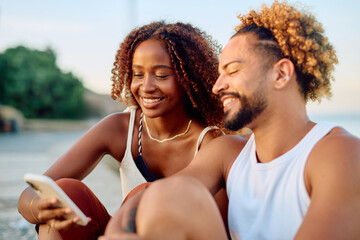 Young couple smiling and bonding while scrolling on a mobile phone, sharing a moment in the summer...