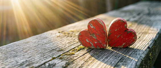 Two rustic red hearts resting on weathered wood bathed in warm golden sunlight.
