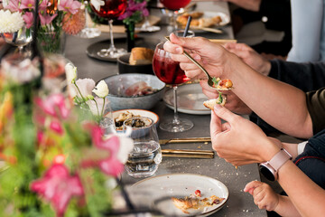 Close-up of hands sharing food and wine at a social table, highlighting togetherness, casual...