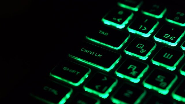 Green backlit keyboard with slow zoom toward the Caps Lock key, representing system state, control and digital interface. Futuristic technology background.