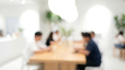 A softly focused interior view reveals a group of people seated around a wooden table possibly in a cafe or office space with