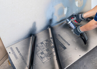 A person wearing protective gloves uses a black aerosol spray paint can with a trigger gun attachment to refinish and restore motorcycle components.