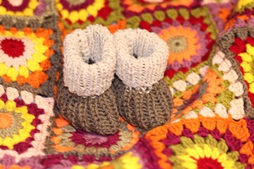Baby knitted booties shoes handmade craft cute little things concept of childhood motherhood cozy home and crocheted colorful blanket beautiful photo