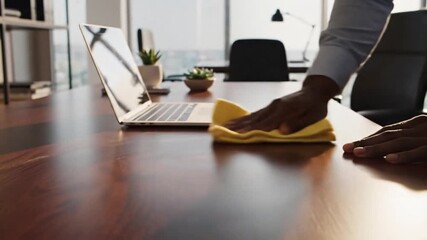 Close up of a man's hand cleaning a modern office desk with a yellow cloth for hygiene concept and a fresh start in a corporate environment