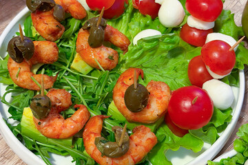 A vibrant dish featuring shrimp and olives on leafy greens, accompanied by skewers of cherry tomatoes and mozzarella. perfect for healthy and visually appealing meals.
