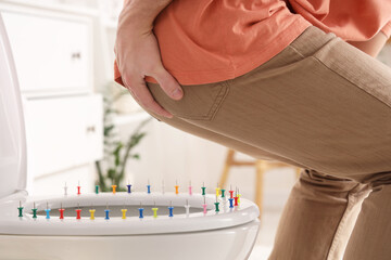 Young man with hemorrhoids and pins on toilet bowl in restroom