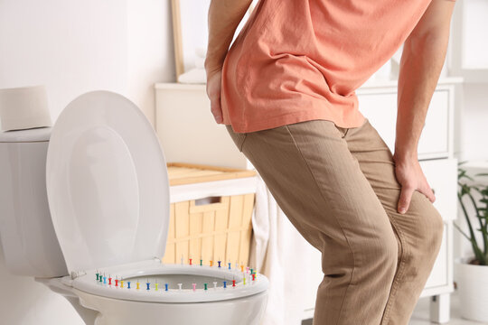Young man with hemorrhoids and pins on toilet bowl in restroom