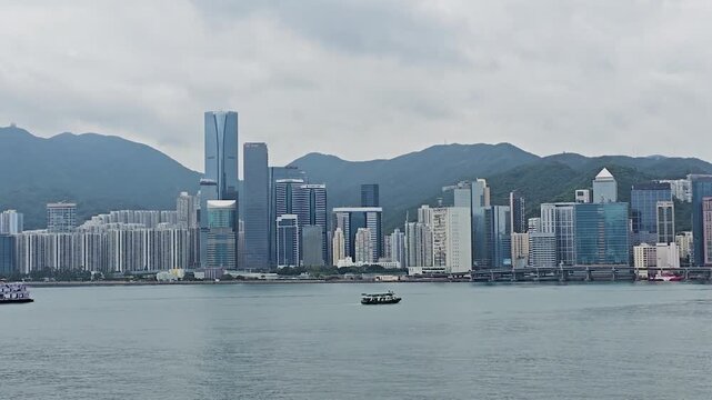 Slow pan sweeping Victoria Harbour's iconic Hong Kong Island skyline from Kowloon, revealing supertall towers like ICC, I Square, and The Cullinan against misty mountain backdrop