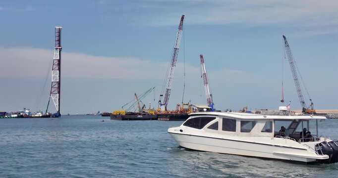 White motorboat with passengers cruising through a harbor with large industrial cranes in the background.