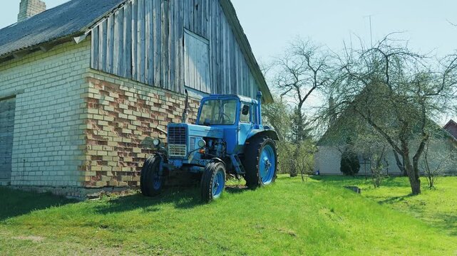 Rural scene showing parked blue tractor beside old farm building in spring