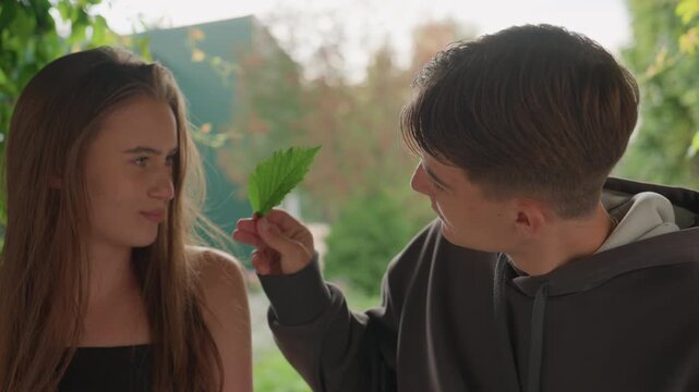 teen couple under ivy sharing leaf, gentle kiss and playful exchange, sunlit garden alcove, boy presents leaf, girl smiles, close intimate portraits capture shy gaze and warm atmosphere