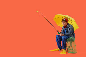 Funny young man in flippers with fishing rod and umbrella sitting on orange background © Pixel-Shot