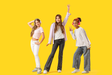 Teenage girls in headphones dancing on yellow background