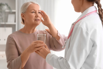 Mature woman taking glass of water from gynecologist in clinic. Menopause concept