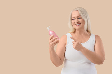 Mature woman pointing at bottle of cream on beige background. Menopause concept