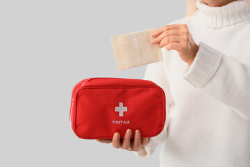 Mature woman putting menstrual pad into first aid kit on light background. Menopause concept