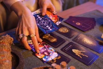 Fortune teller reading tarot cards at table in room, closeup