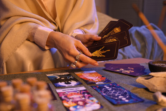 Fortune teller reading tarot cards at table in room, closeup