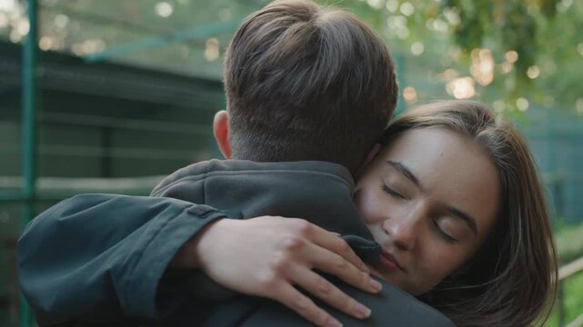 young woman hugging man outdoors gentle reunion in city park with close embrace eyes closed soft jacket warm morning light emotional relief friends and partners reconnecting cinematic shallow depth