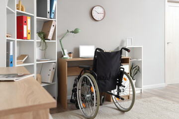 Interior of light office with shelf unit, workplace and wheelchair