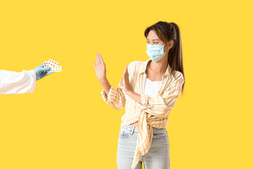 Young woman in medical mask rejecting pills from doctor's hand on yellow background. Immunity...
