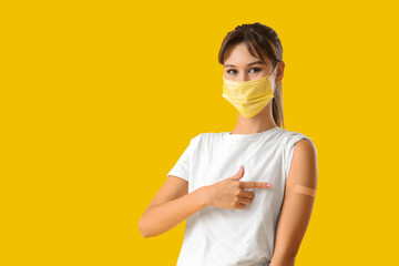 Young woman in medical mask pointing at patch after vaccination on yellow background. Immunity...