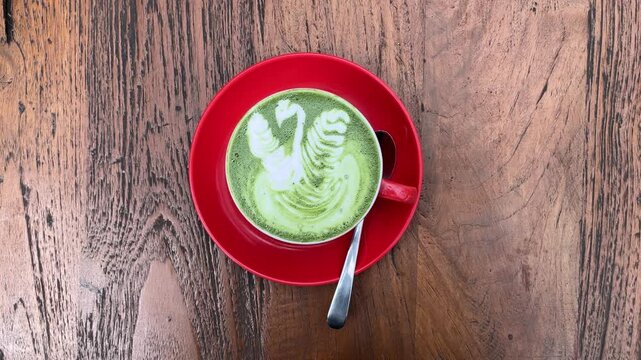 top view of hot matcha latte in the red cup. wooden table on the background. art. swan. wood. brown. nature. isolated. cafe, coffee shop, restaurant. dine in, dining. high angle, above, flat lay. tea 