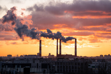 Smoke from factory pipe of heat station in the city in winter time at sunset. Fuel oil or natural gas-fired power plant. Air pollution. Chimneys, ecology, heating season concept. 