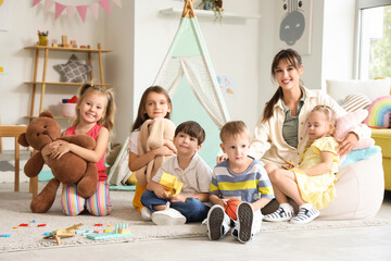 Cute little children with toys and nursery teacher in kindergarten