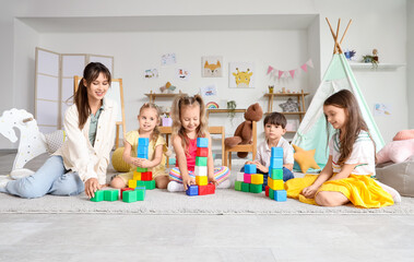 Group of little children and nursery teacher playing with cubes in kindergarten
