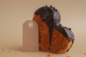 Empty paper note template mock up Heart shaped dark chocolate croissant on beige background with copy space. Puff pastry new trendy sweet dessert bakery. Creamy dough experiment 