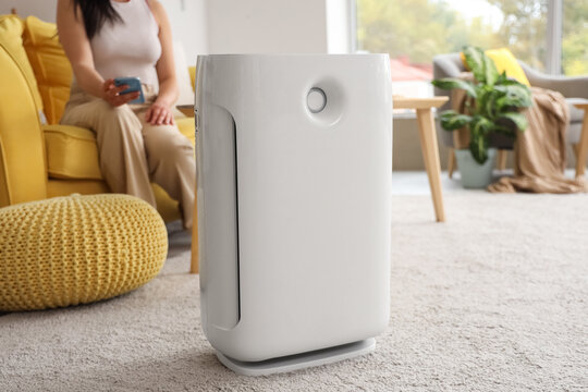 Woman adjusting air purifier using mobile phone at home