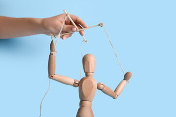 Hand of puppeteer manipulating marionette on blue background
