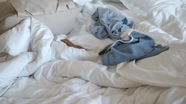 Tossed clothes on a messy bed in a bright room
