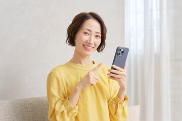 Naklejka premium リビングでスマートフォンを使う女性 ポートレート カメラ目線