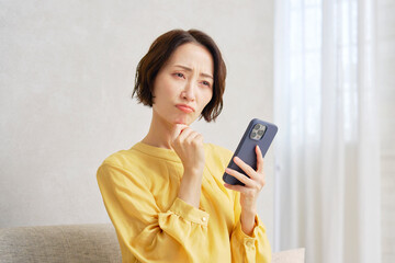 Naklejka premium リビングでスマートフォンを使う女性 悩む