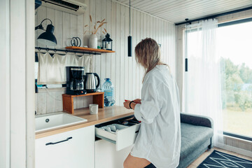woman preparing morning coffee in small modern kitchen interior at home casual lifestyle scene with wooden countertop white cabinets, slow living interior design home comfort