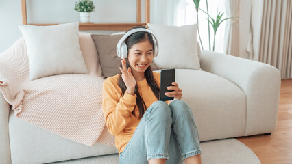 Asian woman listening to music with headphones and mobile phone in living room at home. Headset and sound with song, radio, podcast for motivation and smile