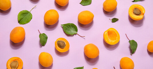 Many ripe apricots and leaves on pink background