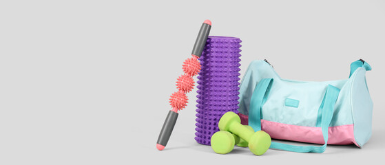Massage rollers with dumbbells and fitness bag on light background