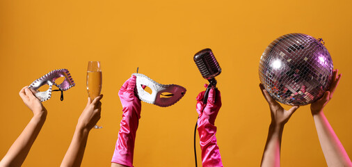 Female hands with disco ball, carnival masks and microphone on orange background